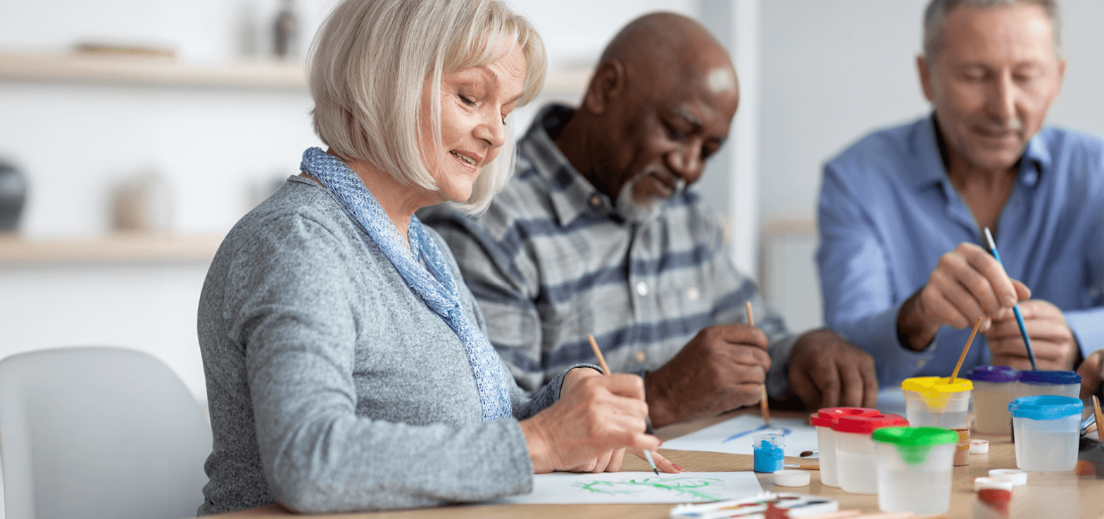 Woman sitting at a table smiling while she and two men paint