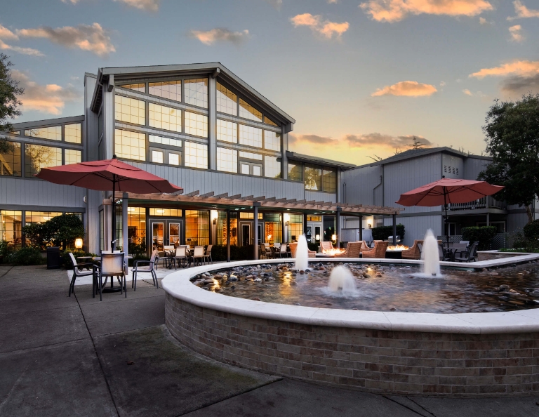 Modern senior community with a large fountain and outdoor seating at sunset.