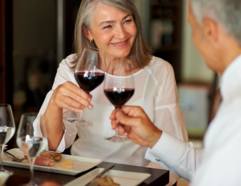 Smiling couple enjoying wine in senior living community dining area.