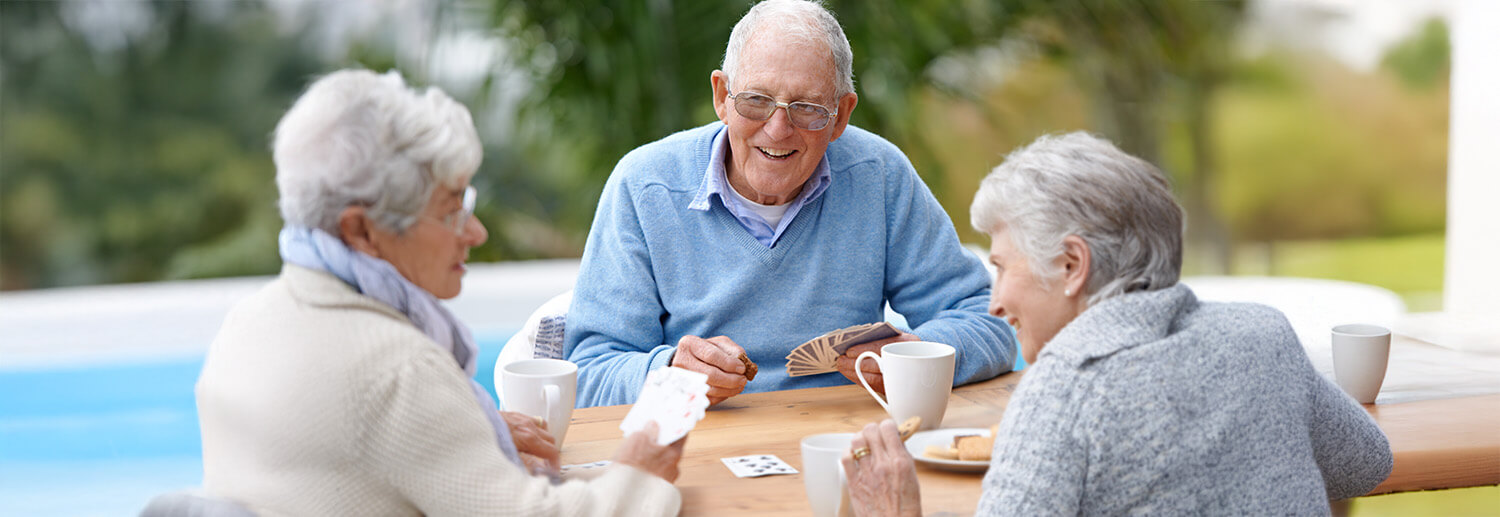 Two older adult women and a senior man smile while playing cards together