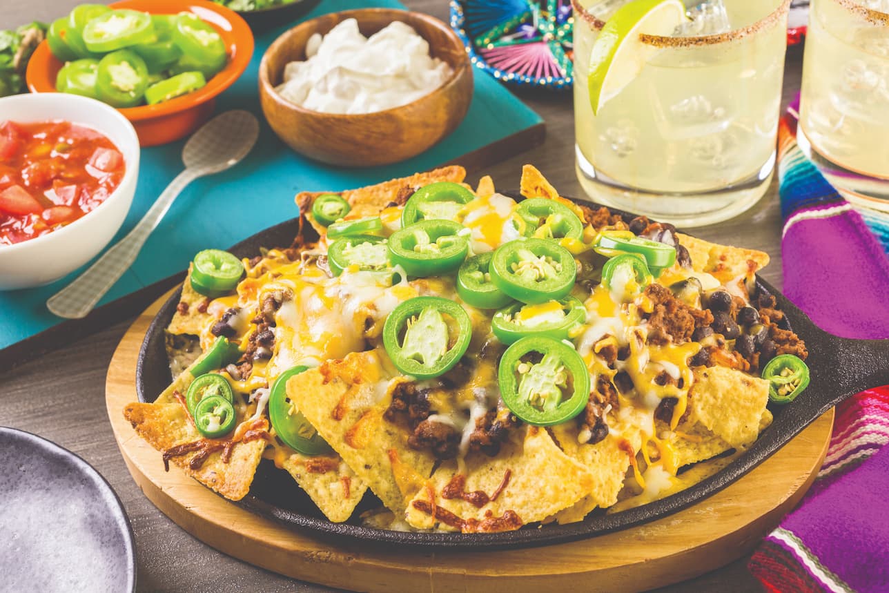 Plate of loaded nachos with toppings and a margarita on the side