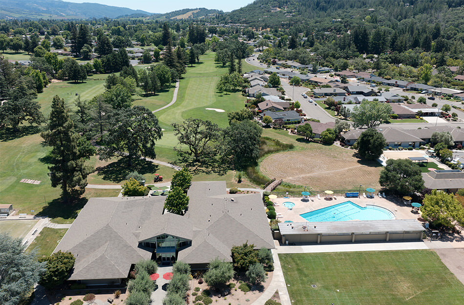 Aerial view of a community center, pool, golf course, and residential units.