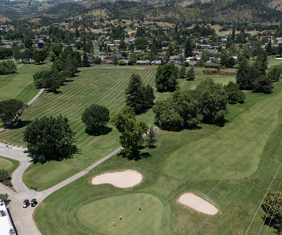 Aerial view of a landscaped golf course near a community surrounded by hills.