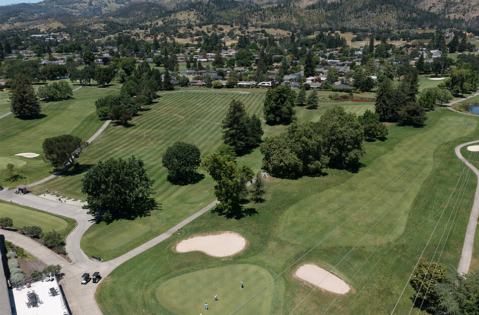Aerial view of a golf course with sand traps and residential units in the background.