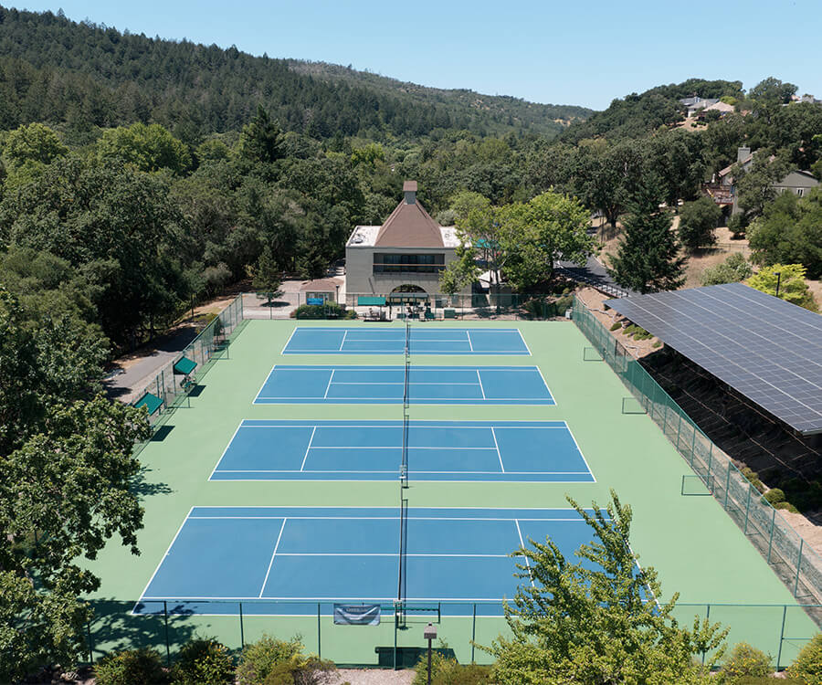 Aerial view of tennis courts in a lush green residential area with solar panels nearby.