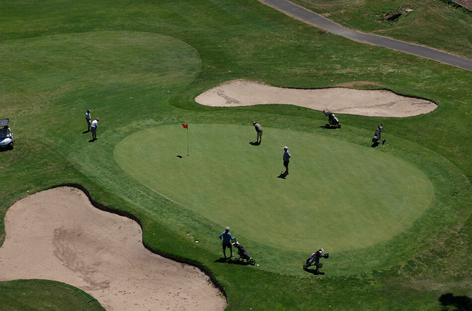 Aerial view of golfers on a putting green with sand bunkers nearby.