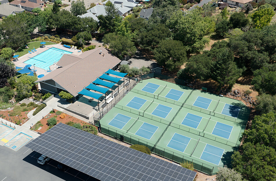 Aerial view of community center with pool and six tennis courts surrounded by trees.