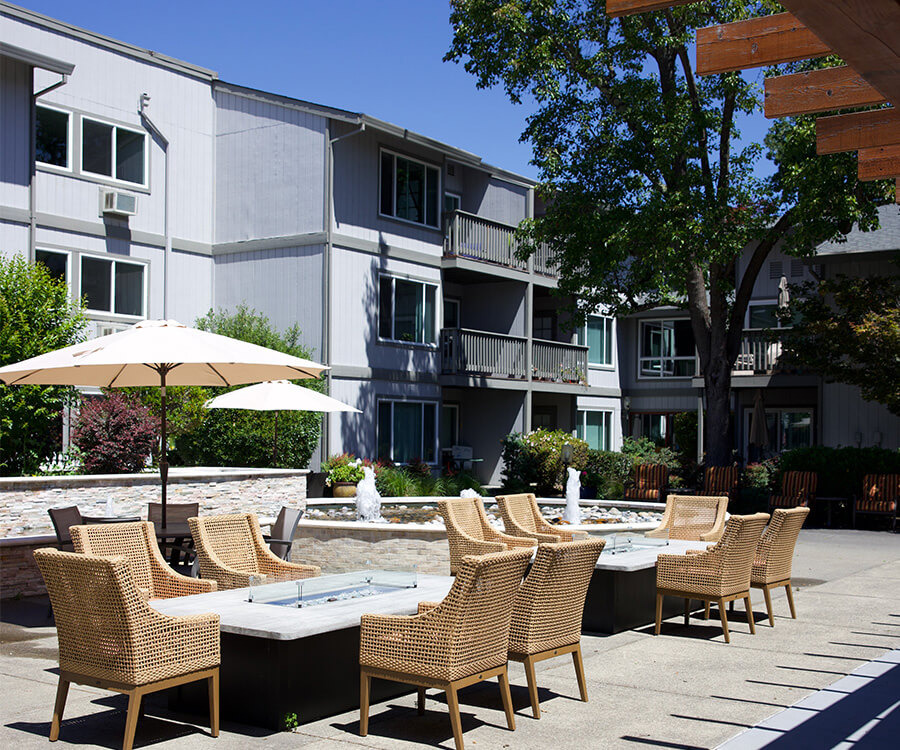 Outdoor patio with wicker chairs, umbrellas, and three-story residential building.