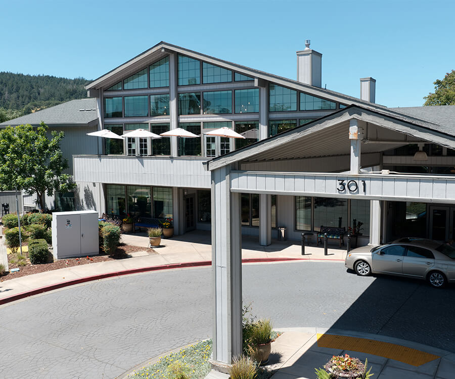 Modern building with large windows and a shaded entrance in a green setting.
