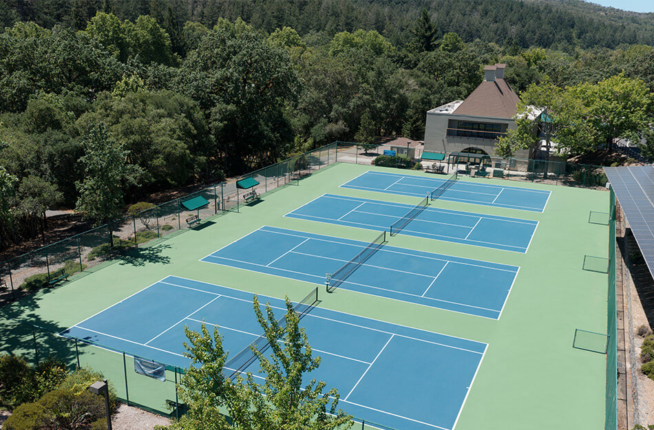 Aerial view of four tennis courts next to a modern building surrounded by trees.