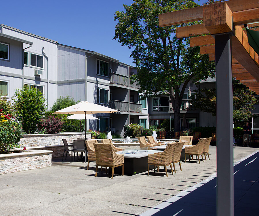 Outdoor seating area with umbrellas and chairs in a senior living community.