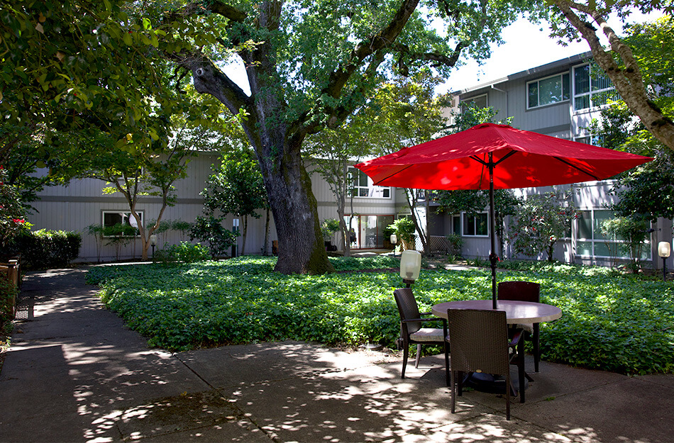 Garden view with red umbrella and seating at senior living community.