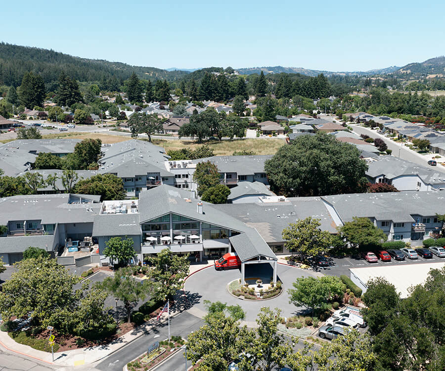 Aerial view of a senior living community surrounded by trees and residential houses.